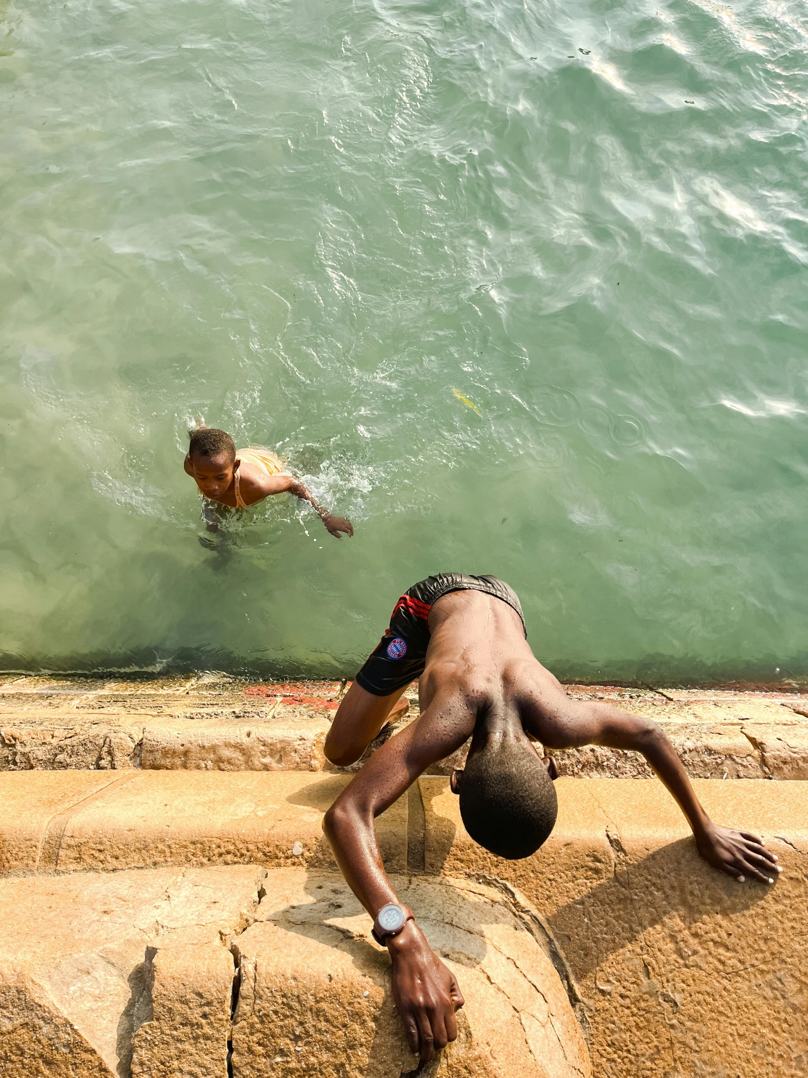 a boy standing at the water's edge with his head under his arm