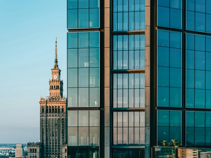 the building is made of glass and a clock tower is shown behind it