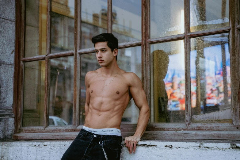 a shirtless man posing by an old window