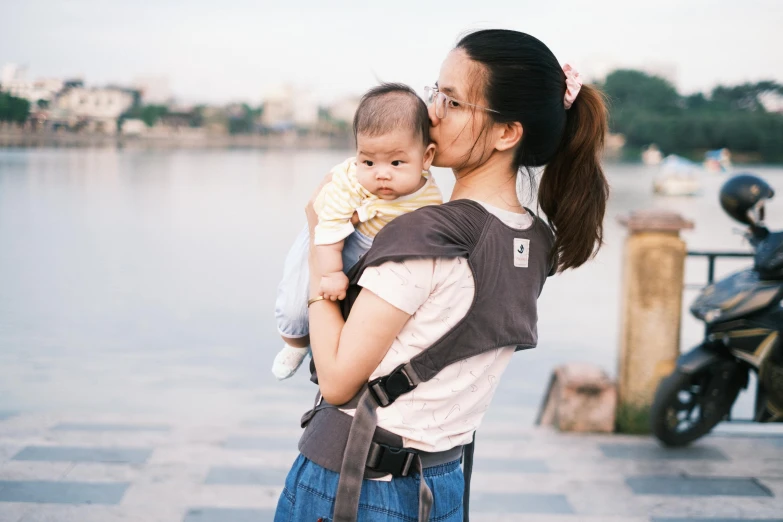 a woman holding a baby standing in front of a body of water