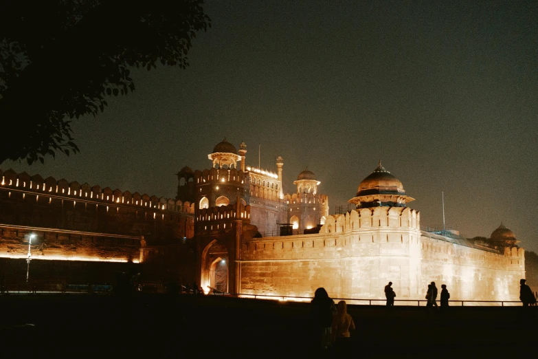 people are gathered near a tall castle at night