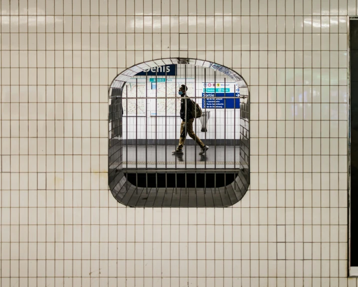 a person walking on a subway platform through a tiled wall