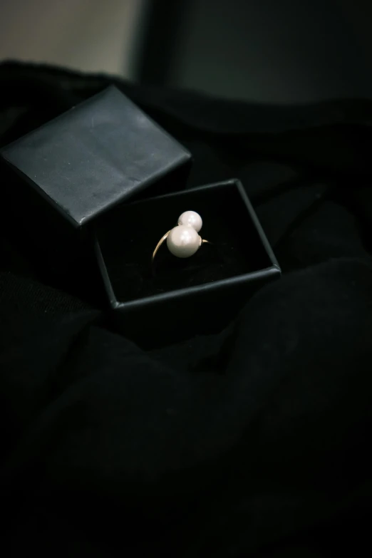 an elegant pearl ring sits inside a small black box