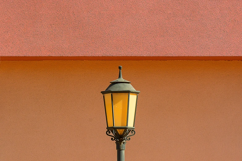 a street light against a brown wall with some pink in it