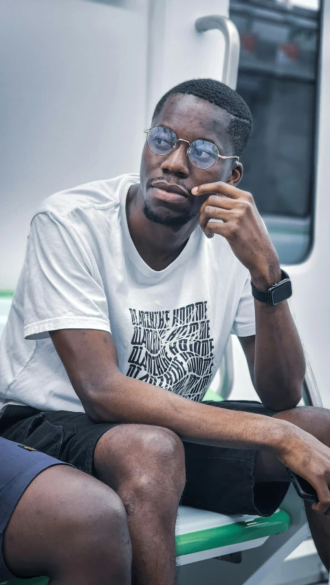 man wearing glasses with a shirt on and a watch sitting on a bench