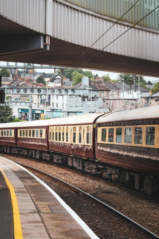 a yellow and brown train under a metal bridge