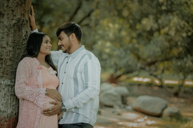 a pregnant couple standing next to a tree