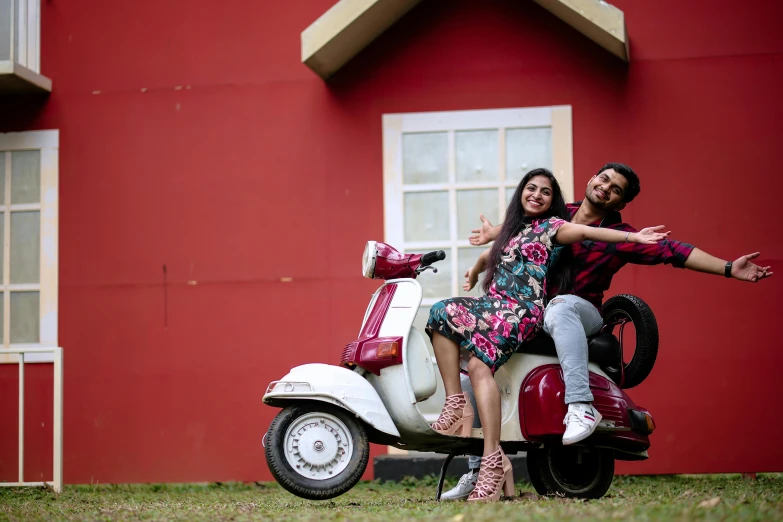 an engaged couple in front of a red building and a white moped