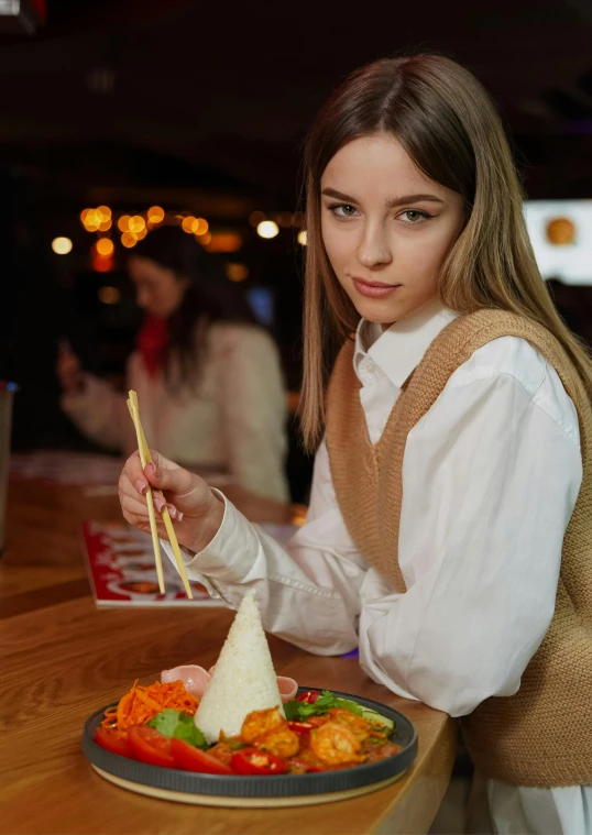 a woman holding chopsticks in one hand and bowl with food on the other