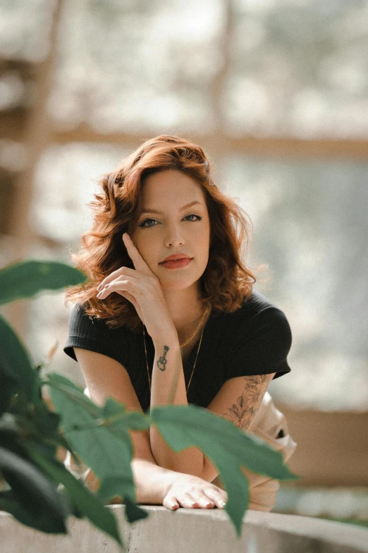 a beautiful red headed woman posing near a green plant