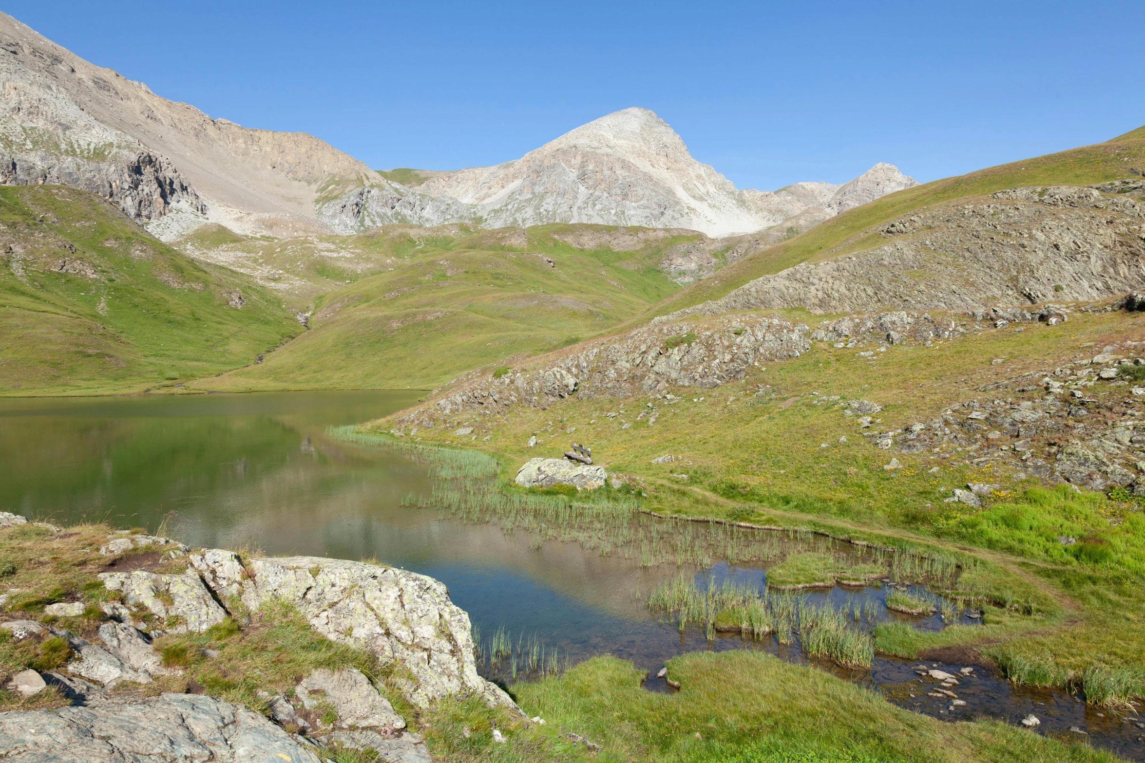 a small pond is at the base of a mountain peak