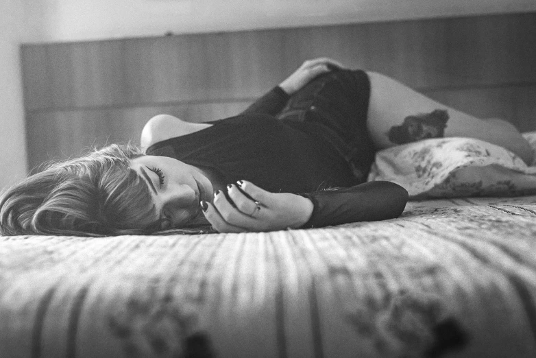 black and white pograph of woman laying on bed with hands touching her face