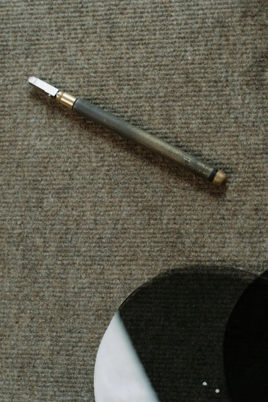 a metal pen laying on a table with a black object beside it