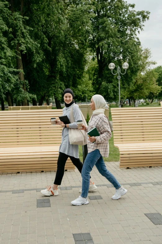 two women walking on a paved walkway in front of benches