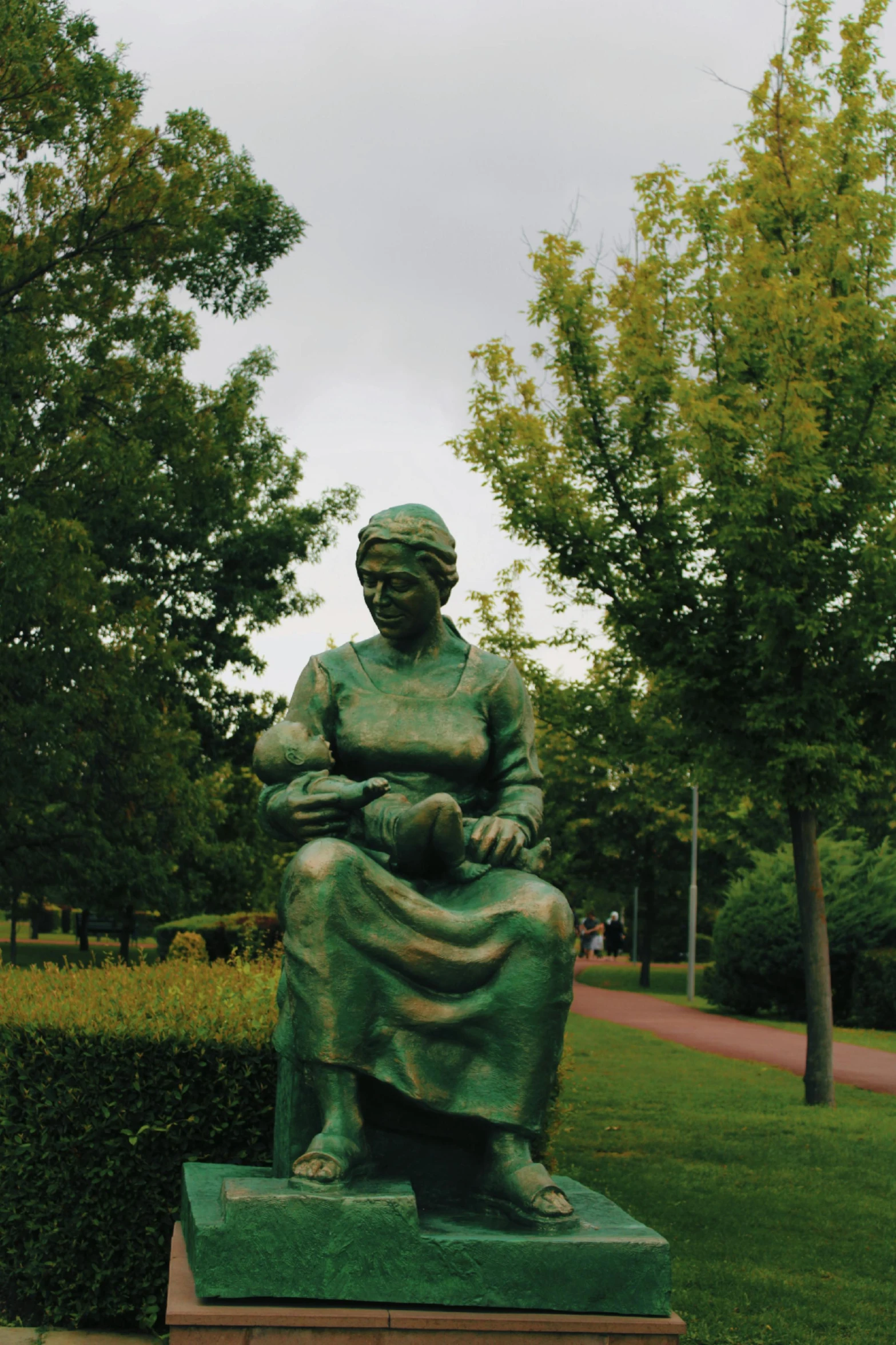 a green statue of a lady with a pot in a park