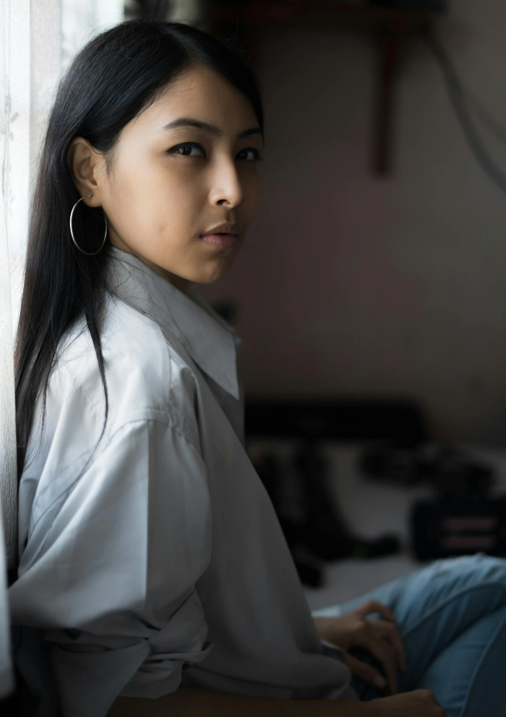 an attractive young asian woman in white sitting on a window sill