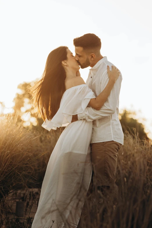 a couple kissing in tall grass with the sun peeking over them