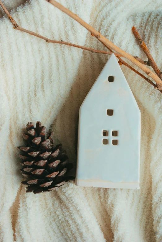 a small white house ornament next to some cones on a blanket