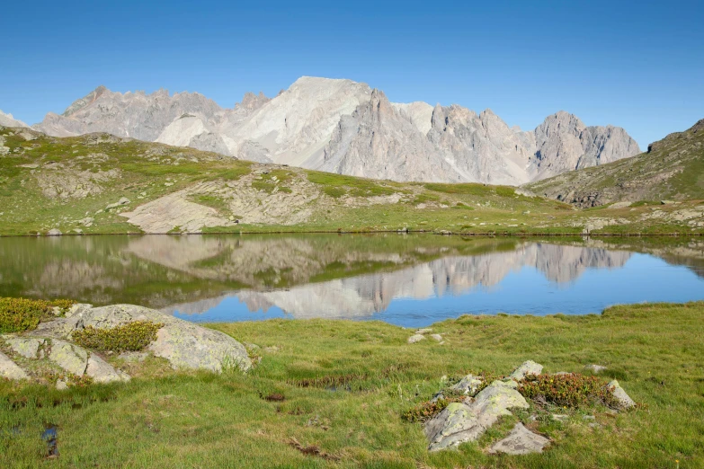 a mountain range with the water in the foreground and a grassy field around it