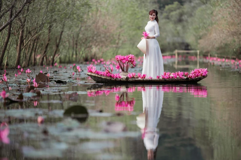 woman in white dress and long skirt standing in boat filled with pink flowers