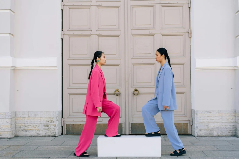 two women wearing pink suits and blue are standing on a block