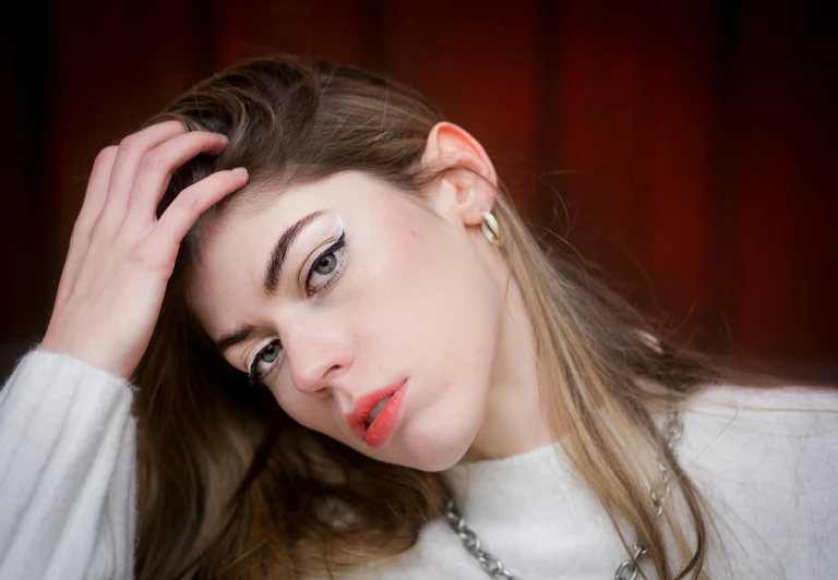 young woman in white sweater holding her head next to the camera