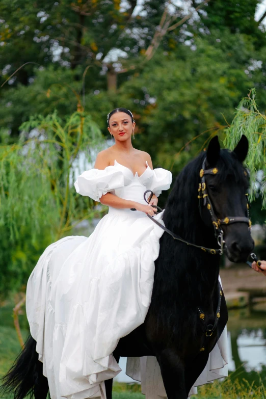 a woman wearing a white dress riding on the back of a black horse