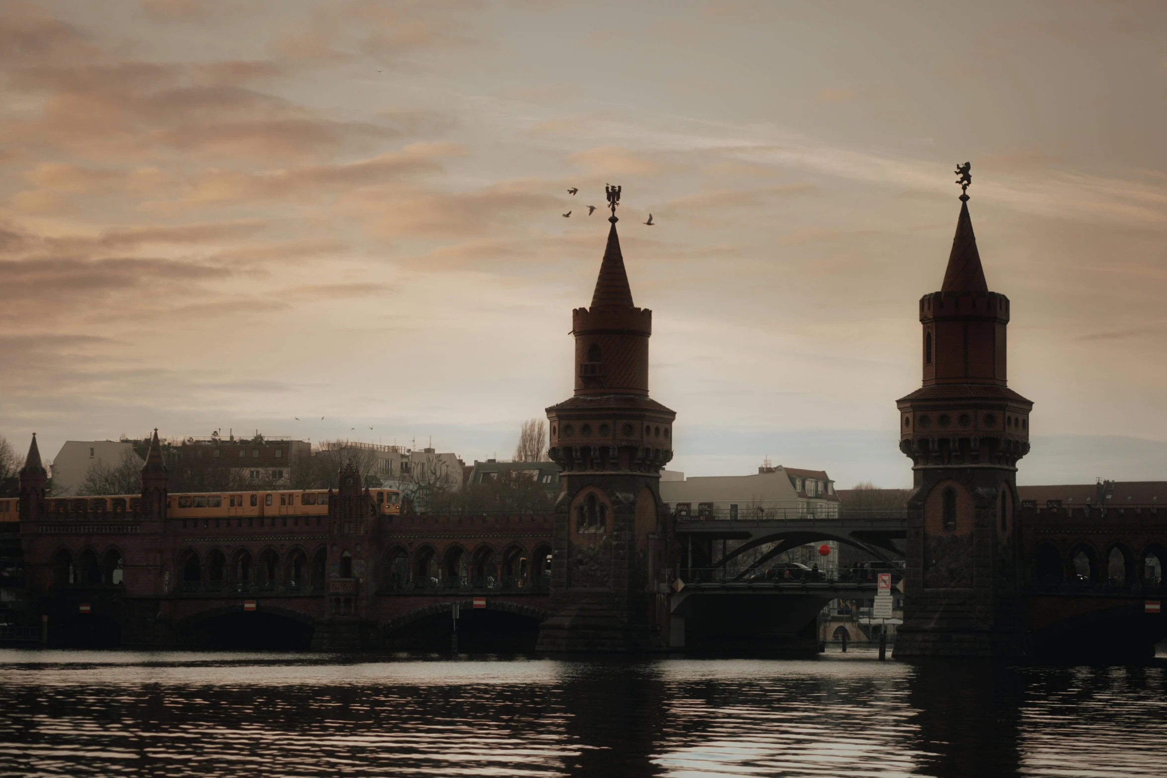 two spires are seen over the water in front of a bridge