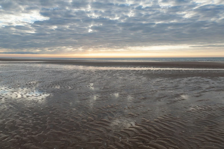 clouds are reflected in the wet sand at the beach