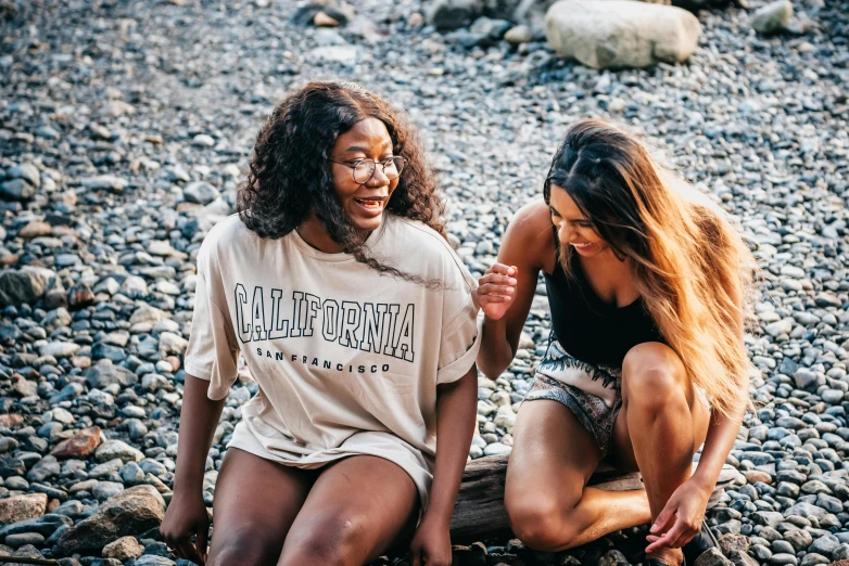 two women are sitting on a stone beach