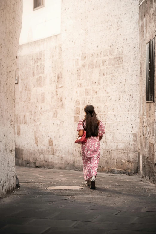 a woman walking down an alley way near some tall buildings