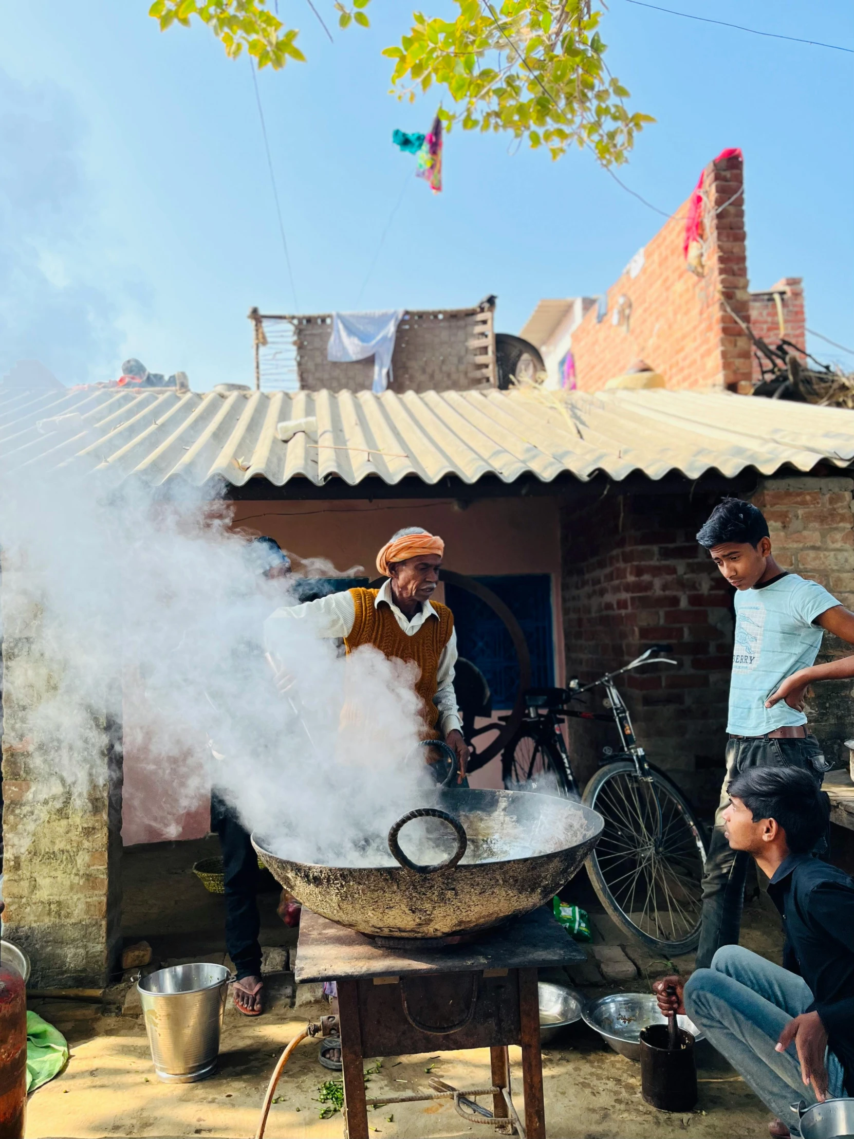 several young men cooking food outside while on bicycles stand by