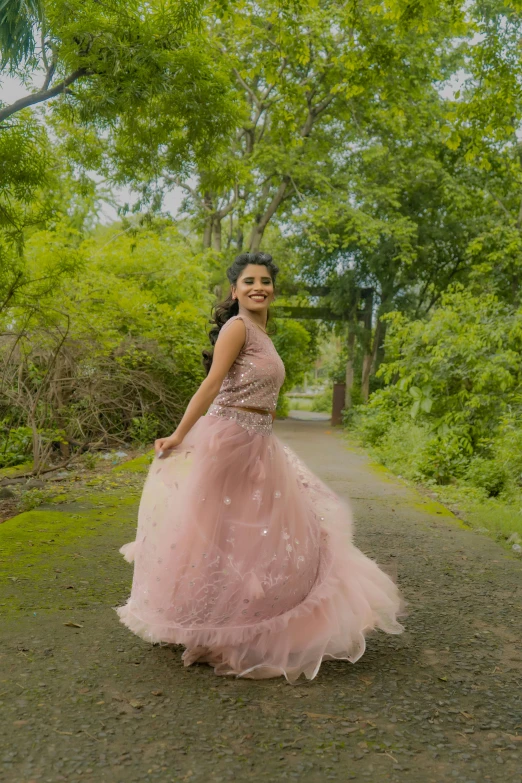 a beautiful young woman wearing a pink dress and standing on a dirt road