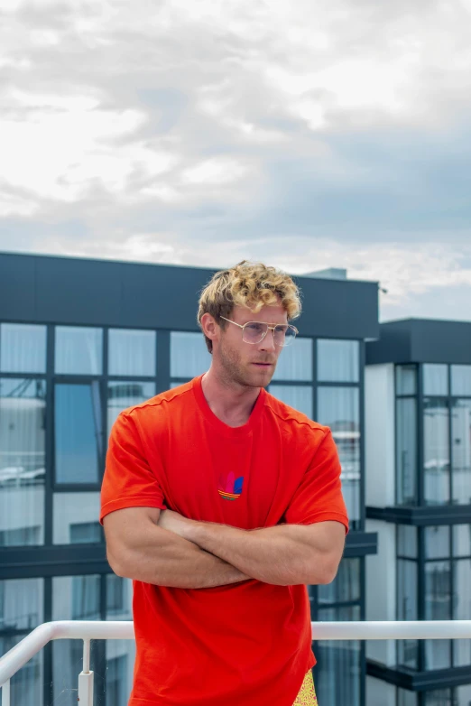 man in red shirt with crossed arms in front of buildings