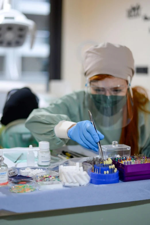 a woman in medical clothing and gloves working on dental instruments