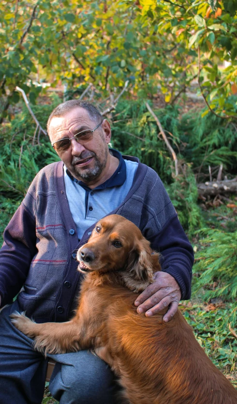 a man kneeling down with a dog in his lap