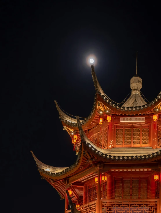 an oriental building illuminated with the moon behind it