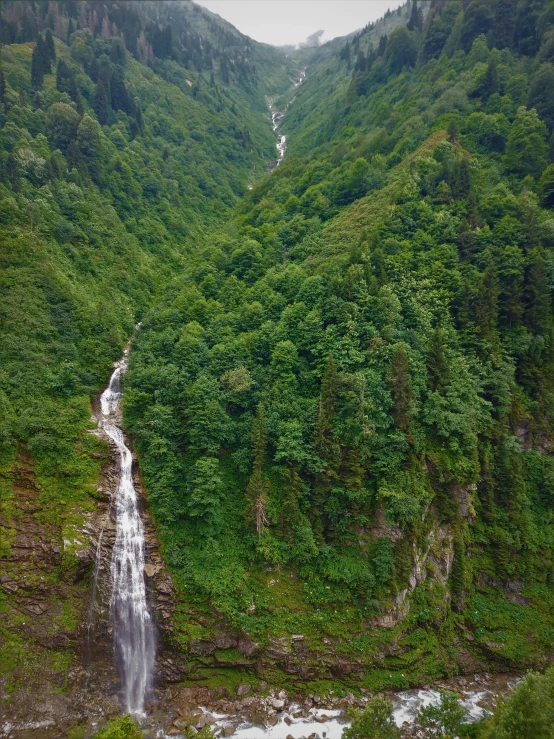 a waterfall in a large valley is near a lush green hillside