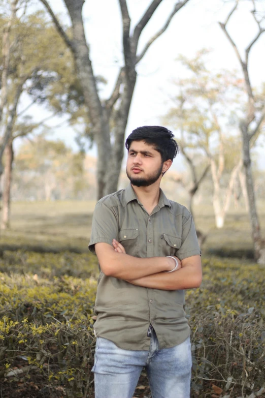 a man standing in front of trees with his arms crossed