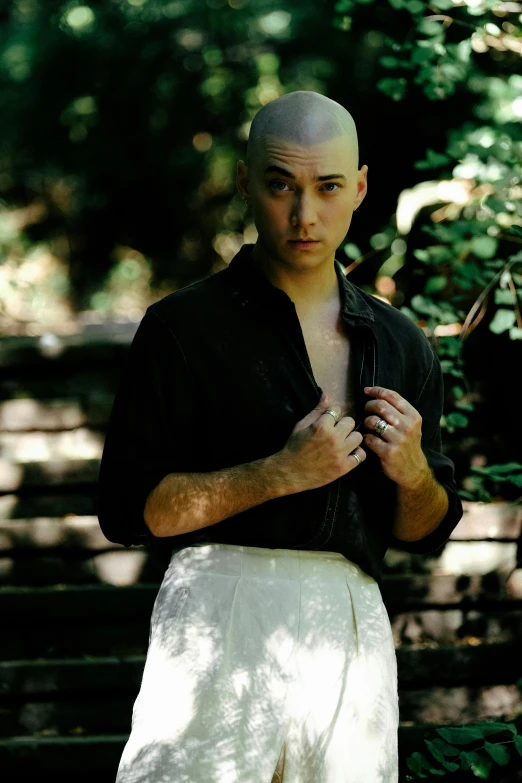 a young man wearing white pants standing in front of some trees