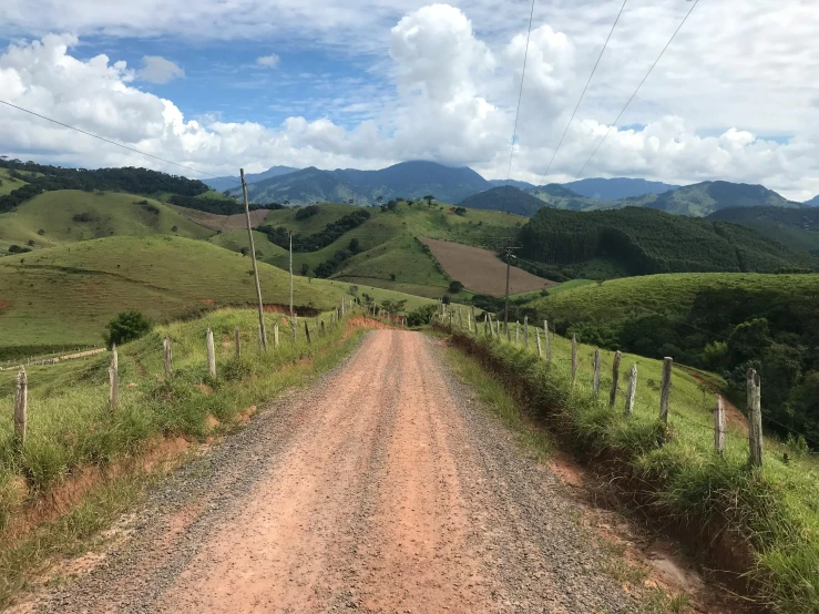 an empty dirt road stretches over a green hillside