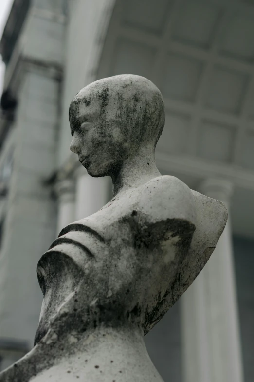 statue of female head facing right, sitting outside a building