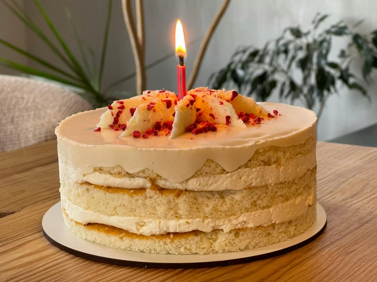 a cake on a wooden table has a single lit candle