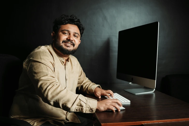 a man poses at a desk next to a computer