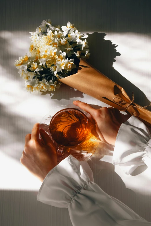 the image of an unrecognized hand holding a glass next to a bouquet of daisies