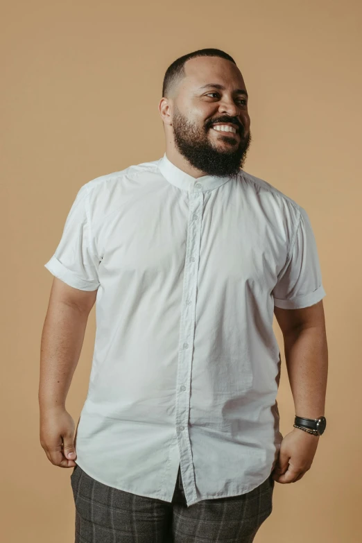 a man with a beard standing in front of a tan wall