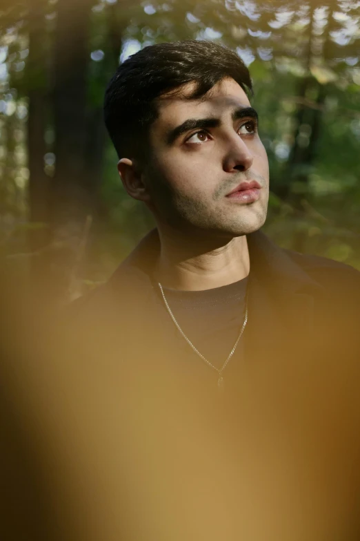 a man looking upward with a forest behind him