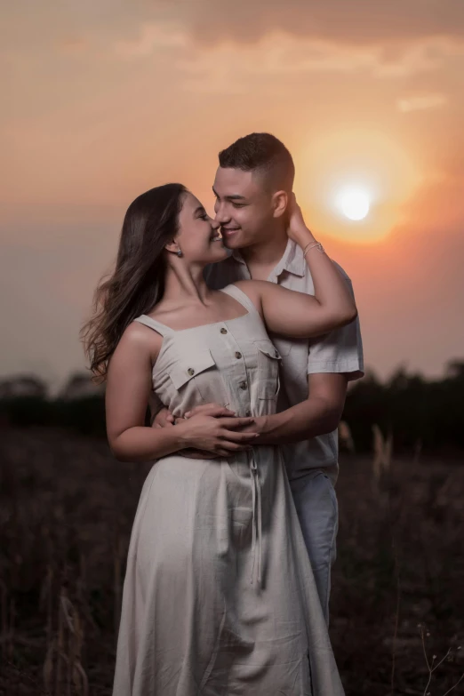 a man and woman kissing in a field at sunset