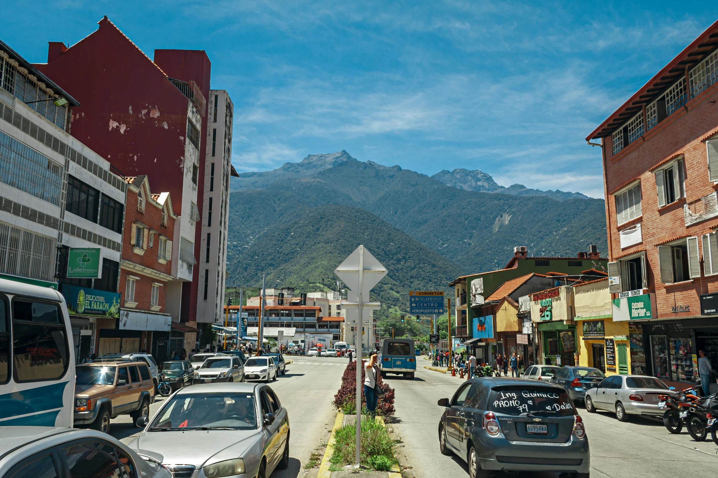 a busy city street has parked cars in front of a mountain