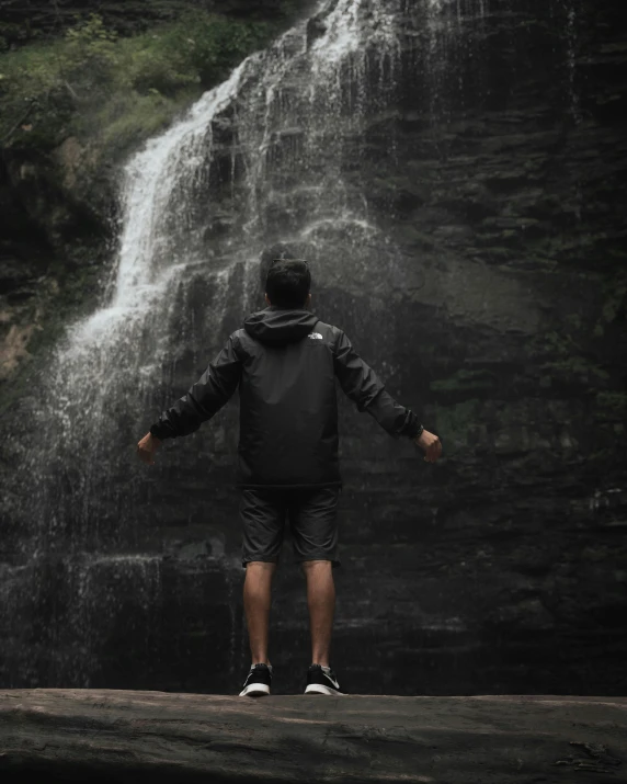 a man in shorts stands with his hands in front of a waterfall